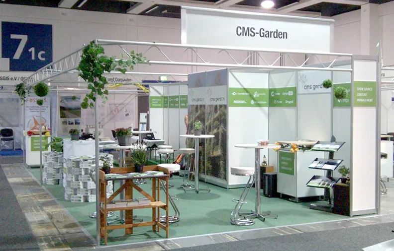 Green carpet, back walls with white CMS logos on a green band, garden photos, artificial flowers, a garden work table