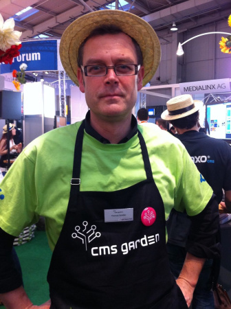 Portrait eines Mannes in hellgrünem T-Shirt mit Strohhut. Seine Gärtnerschürze zeigt ein CMS-Garden-Logo.