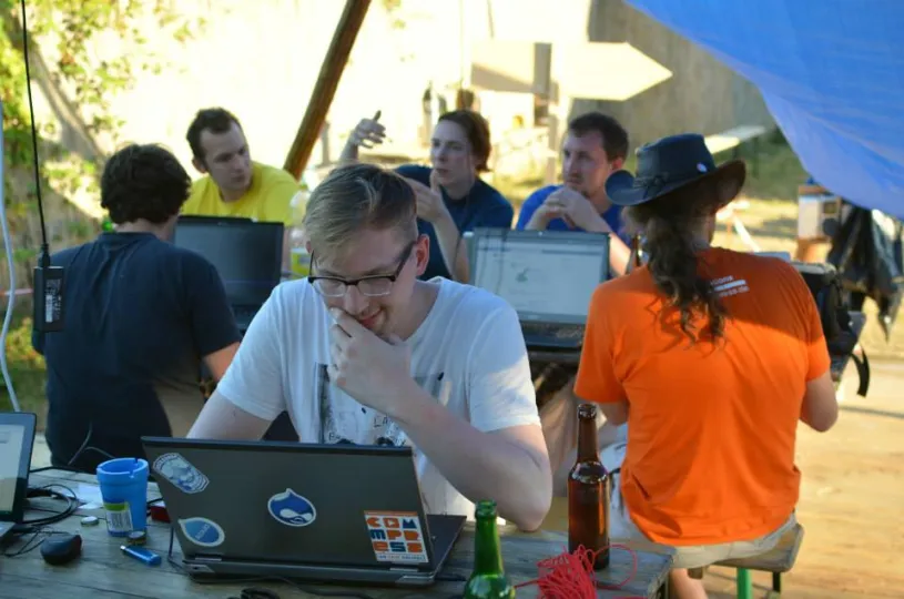 Some people in colorful t-shirts working at their laptop computers in the shadow on a bright sunny day