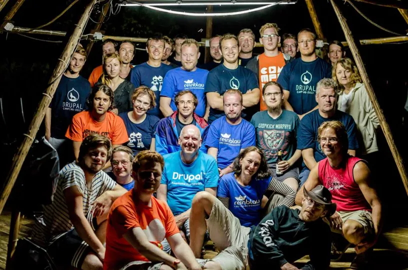 Attendees in colorful t-shirts posing for a group photo at night, lit by a spotlight