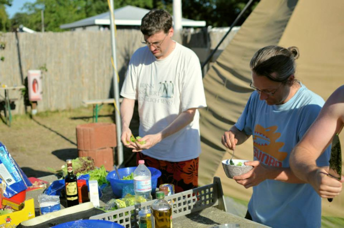 Zwei Männer bereiten auf einer Tischtennisplatte verschiedene Speisen zu