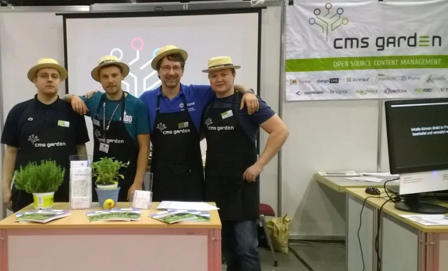 Am Messestand vom CMS Garden legen posieren vier Männer mit Strohhut, die Arme um die Schultern der Kollegen gelegt