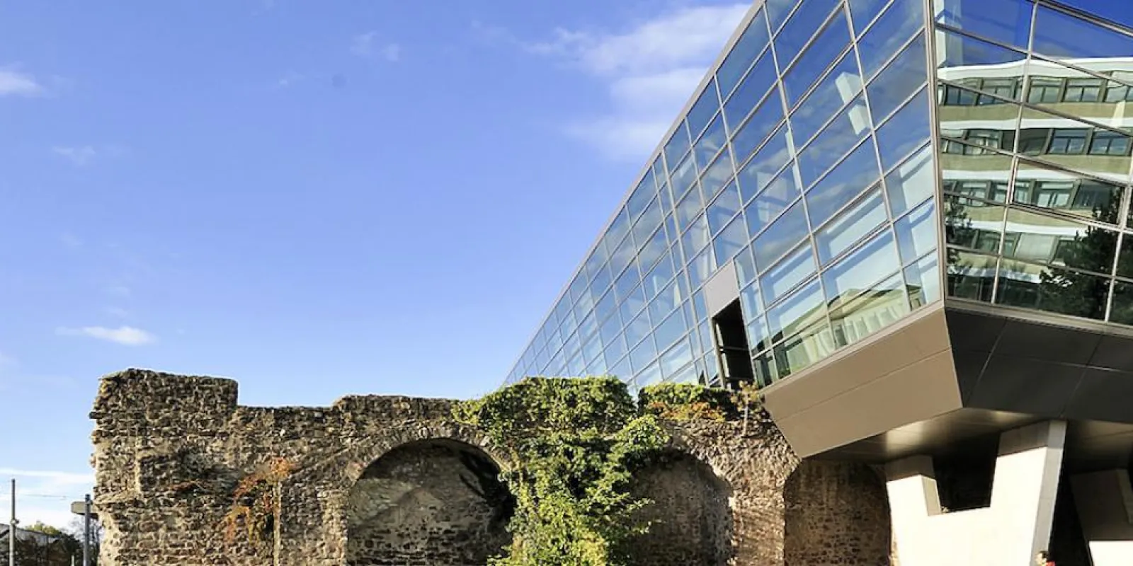 A modern multi-angled building with an all-glass facade side on side with antique roman ruins