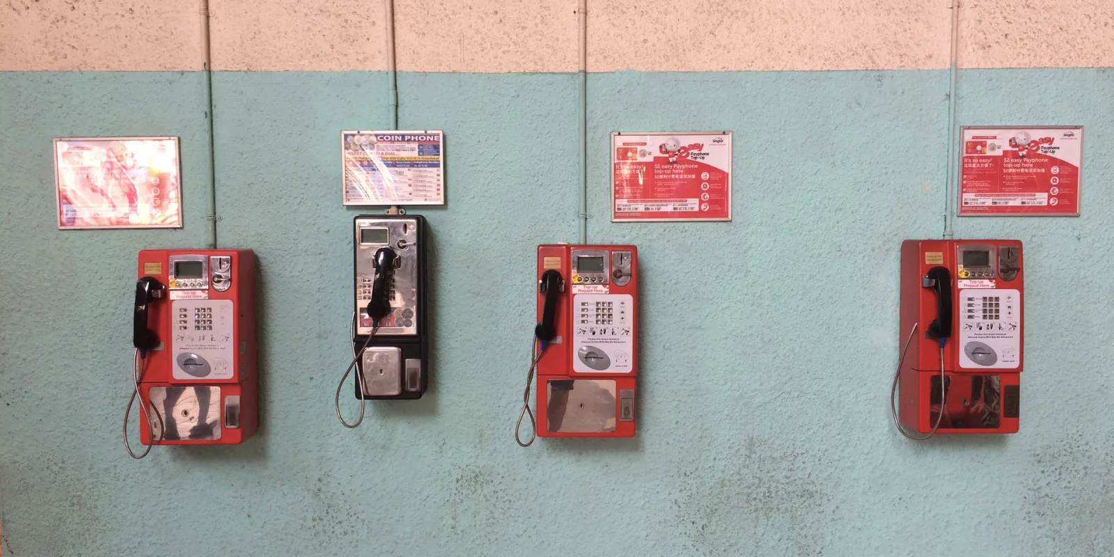 Four different phone boxes are mounted in slightly different heights on shabby turquoise wall