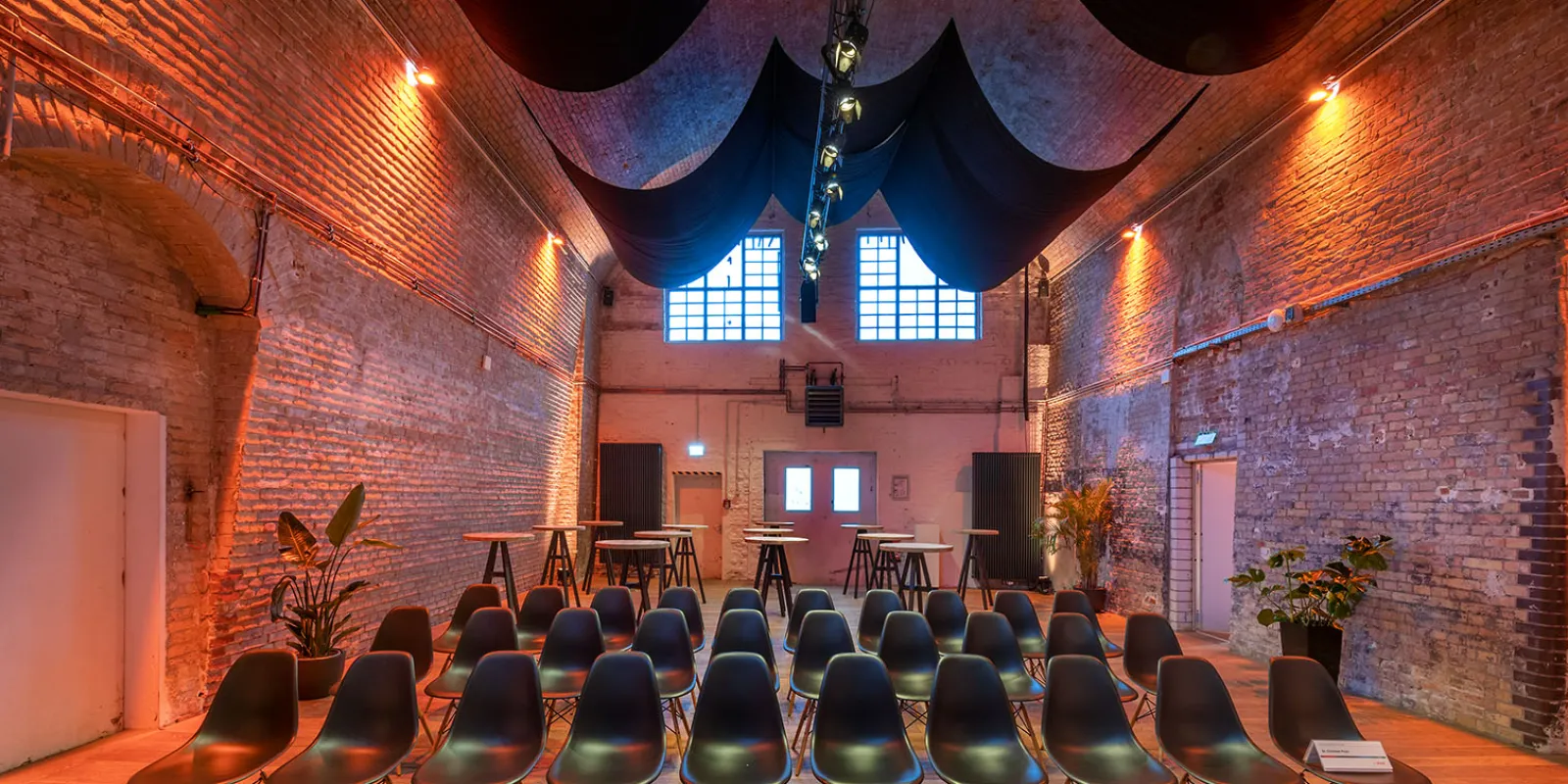 Audience seats on a wooden floor in a warm lit room with bare brick wall