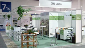 Green carpet, back walls with white CMS logos on a green band, garden photos, artificial flowers, a garden work table