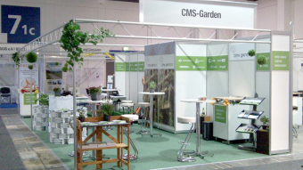 Green carpet, back walls with white CMS logos on a green band, garden photos, artificial flowers, a garden work table