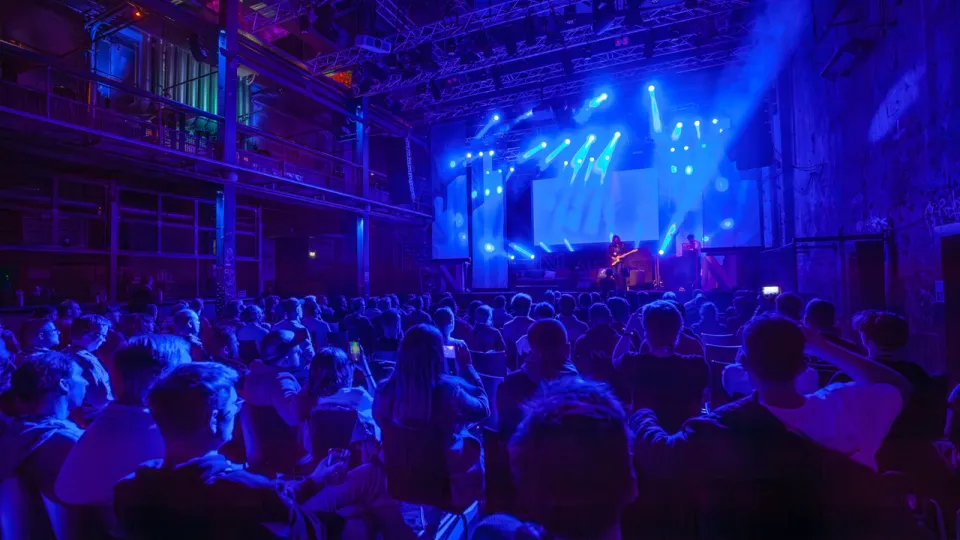 Audience bathed in dim blue light, looking at a stage with two musician